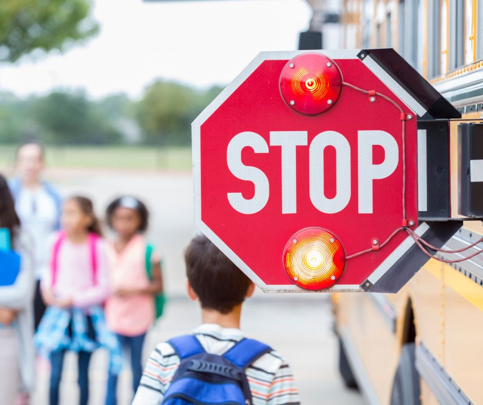 school bus with stop sign out and lights on as kids enter the bus